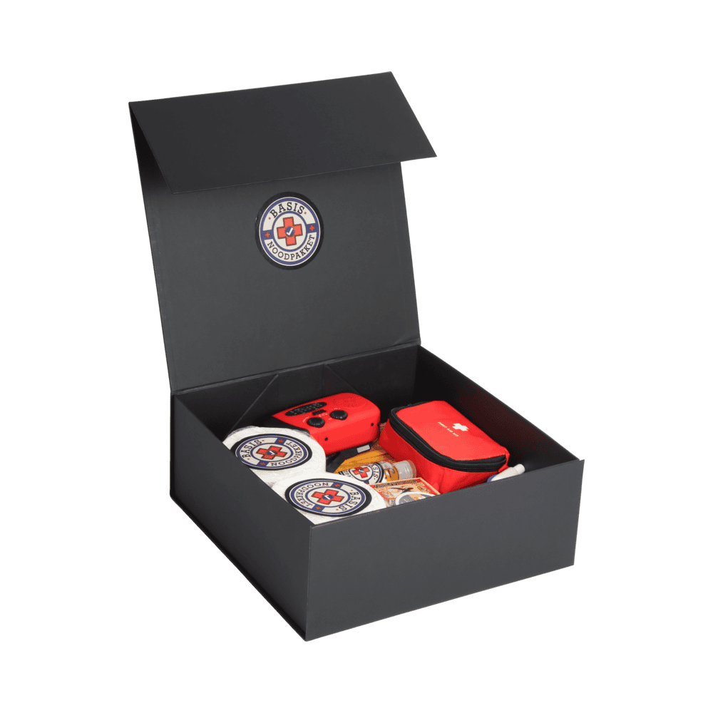 Zwarte doos met open deksel, gevuld met noodpakketinhoud zoals EHBO-set, kaarsen en radio.